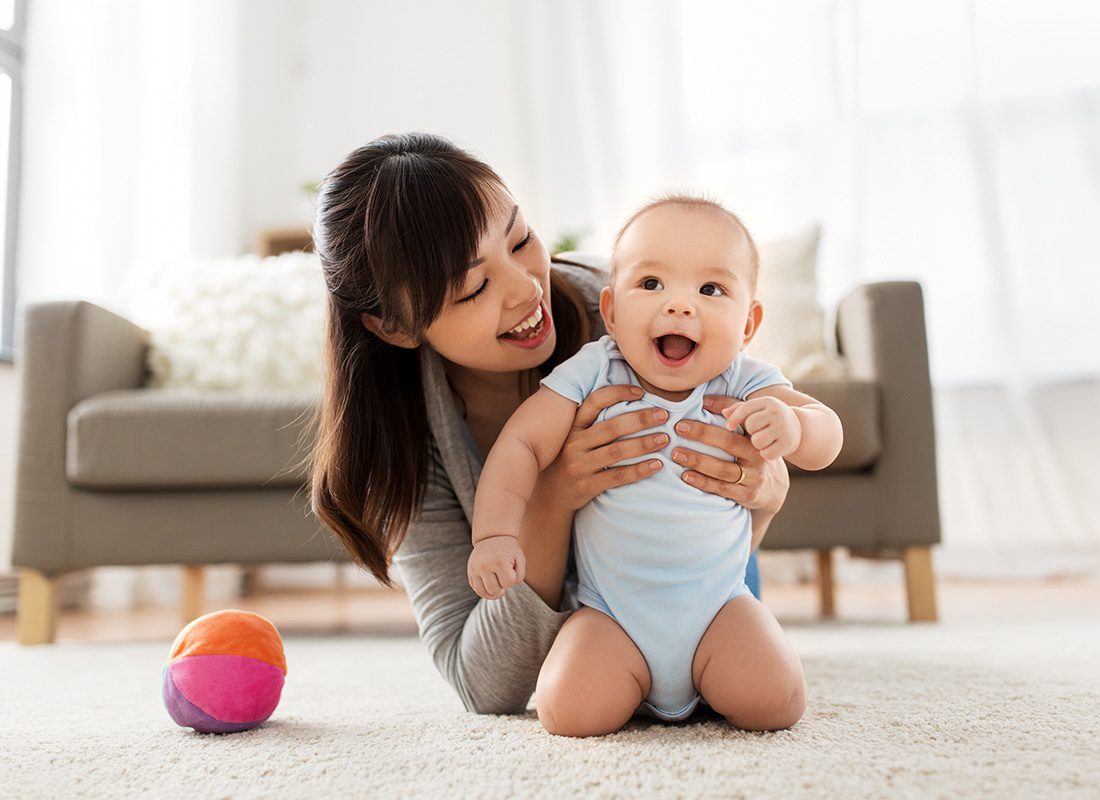 Life Insurance - Portrait of a Cheerful Young Mother Having Fun Playing with her Baby on the Carpet in the Living Room