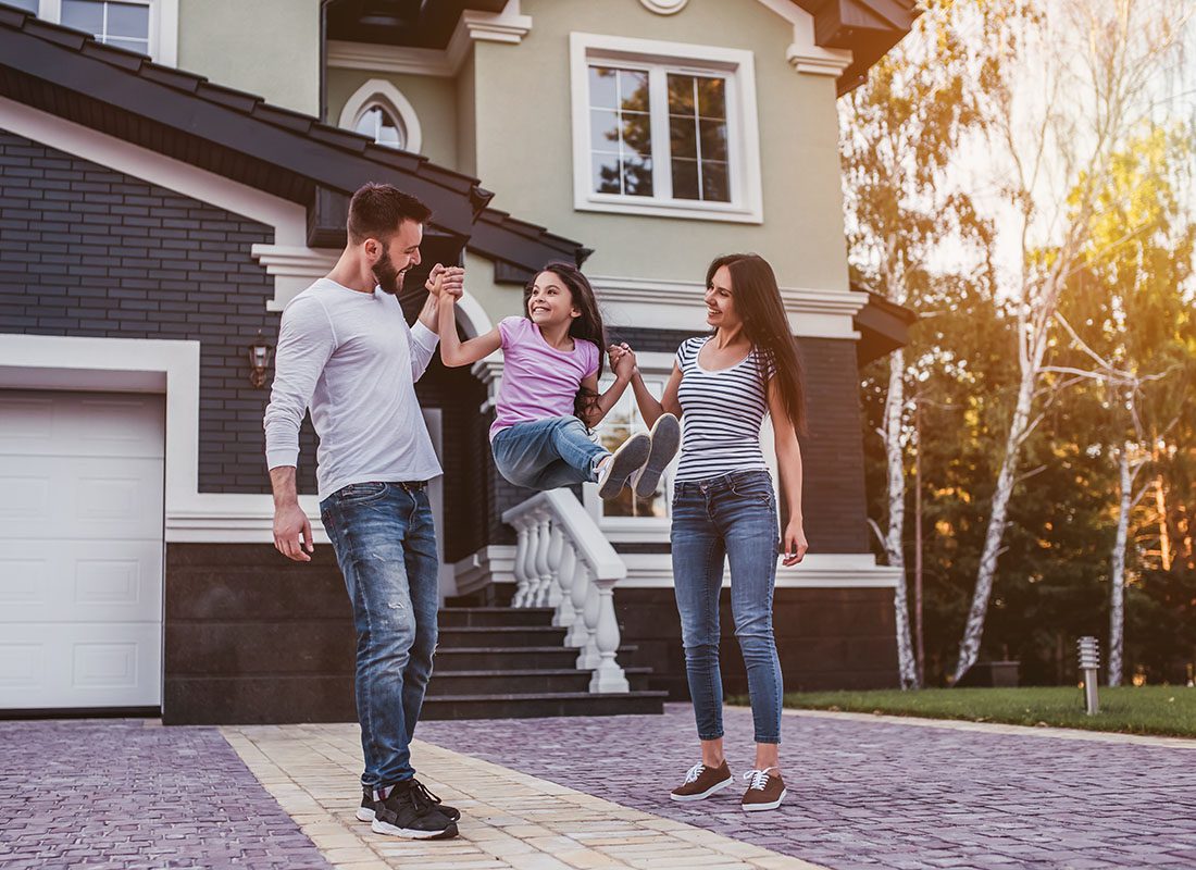 Personal Insurance - Portrait of Cheerful Young Parents Having Fun Holding Up Their Daughter in the Air as They Stand in Front of Their New Home on a Sunny Day